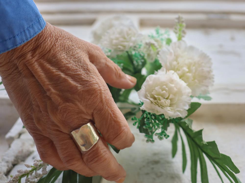 Vanha käsi laskemassa kukkia arkulle.